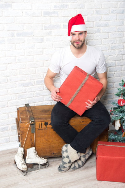 Winter holidays, fun, sports. Macho in red hat hold wrapped present. Gift giving and exchange. Man santa with skates and boxes at christmas tree. Boxing day concept. - Fotoğraf, Görsel