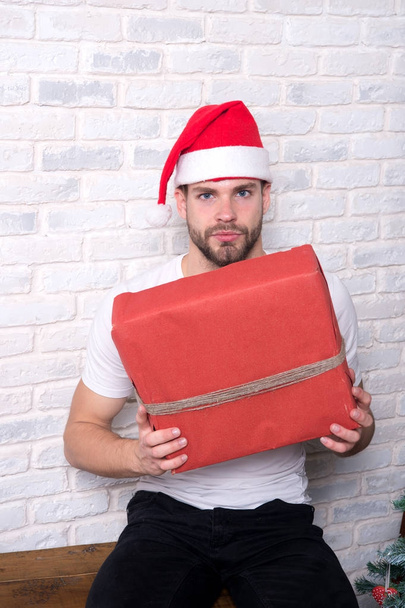 Boxing day concept. Man santa with red box on white brick wall. Macho in christmas hat hold wrapped present. Gift giving and exchange. Holidays preparation and celebration. - Foto, Bild