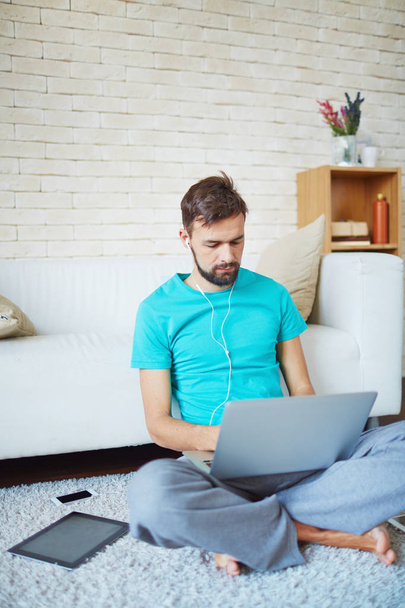 Súlyos fiatal vállalkozó üzleti futás otthon: ő gépelés-on laptop és ferde kanapén ülve, a padló - Fotó, kép