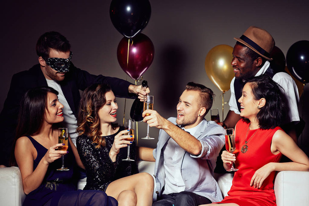Groupe multi-ethnique d'amis réunis à la fête à la maison et s'amusant, ils tenant flûtes à champagne dans les mains
 - Photo, image