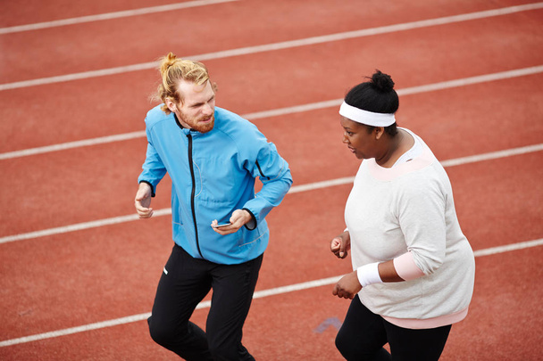 Genç eğitmen ve tombul kadın birlikte maraton rekabet önce stadyum yarış pisti üzerinde koşu - Fotoğraf, Görsel