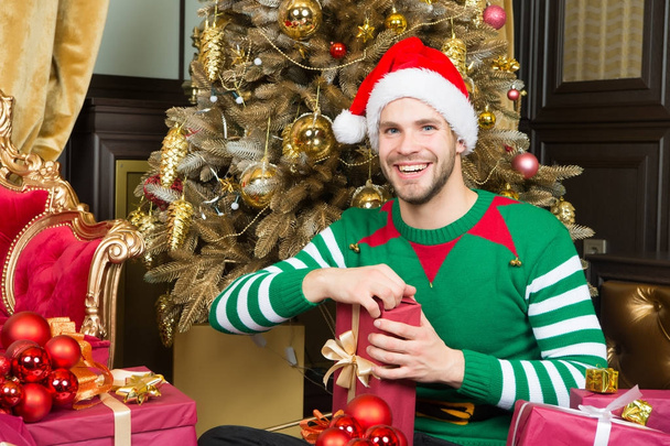 Man in santa hat smile with presents at Christmas tree - Foto, Imagen