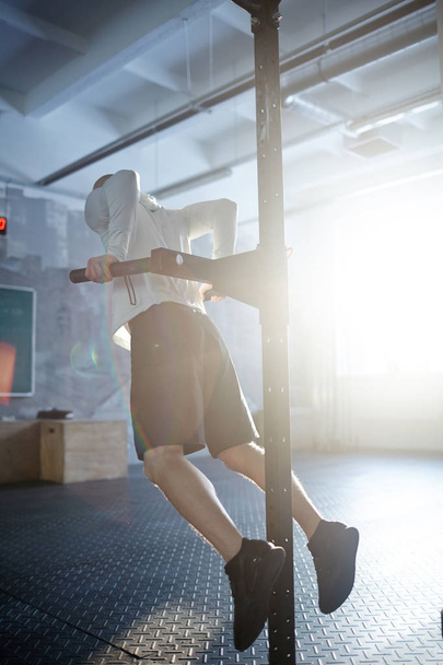 Vista posteriore dell'uomo muscoloso che fa esercizi di pull up sul rack monte in palestra illuminata dal sole
 - Foto, immagini