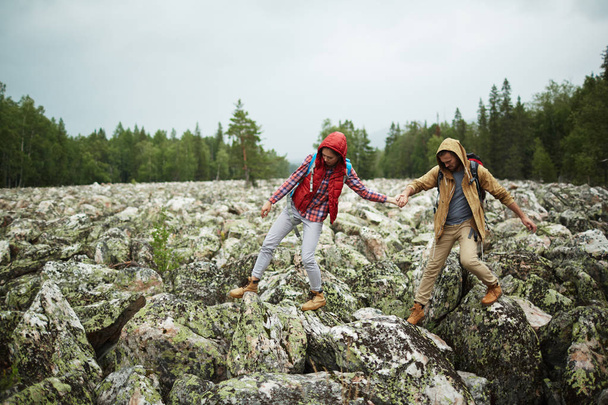 Jóvenes turistas caminando por grandes piedras mientras caminan
 - Foto, Imagen