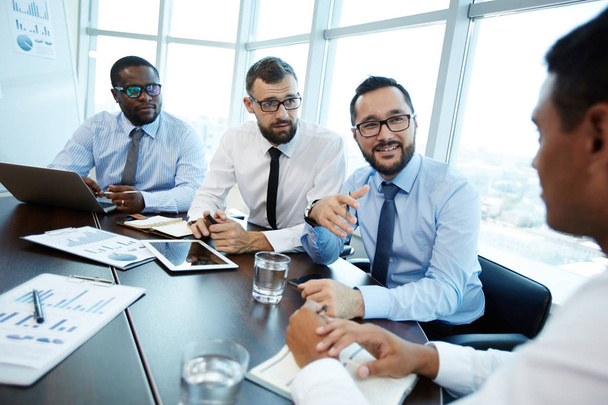 Três funcionários barbudos em óculos conduzindo negociações com seu parceiro de negócios enquanto sentados na moderna sala de reuniões
 - Foto, Imagem