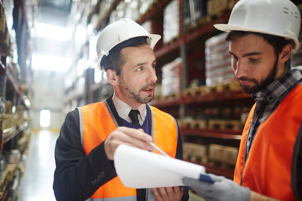 Supervisor in helmet pointing at document while talking to one of managers - Photo, Image