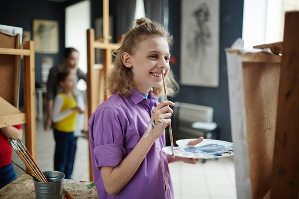 Счастливый школьник с акварелью и кистью, смотрящий на свою картину
 - Фото, изображение