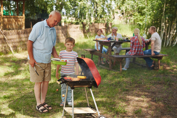 Little boy and his grandfather roasting barbecue at picnic - Photo, Image