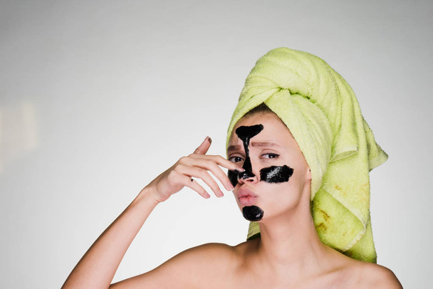 Młoda dziewczyna z zielony ręcznik na głowie stosowane czarne oczyszczanie maski do obszarów problemowych - Zdjęcie, obraz