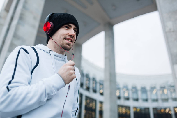 Tipo deportivo escuchando música en auriculares mientras se ejecuta en el entorno urbano
 - Foto, imagen