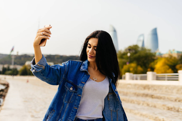 black-haired stylish girl travels through Azerbaijan, makes selfie on the background of modern buildings in Baku - Φωτογραφία, εικόνα