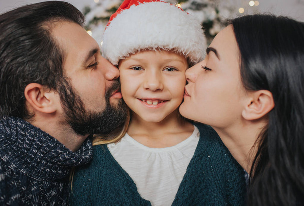 Merry Christmas and Happy Holidays Cheerful Mother, father and her cute daughter girl exchanging gifts. Parent and little child having fun near Christmas tree indoors. Morning Xmas. Portrait family - Foto, imagen