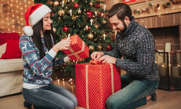 Merry Christmas and Happy New Year . Young couple celebrating holiday at home. Man and woman unpack gifts - 写真・画像