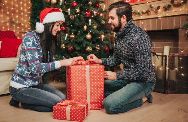 Merry Christmas and Happy New Year . Young couple celebrating holiday at home. Man and woman unpack gifts - Foto, Imagen