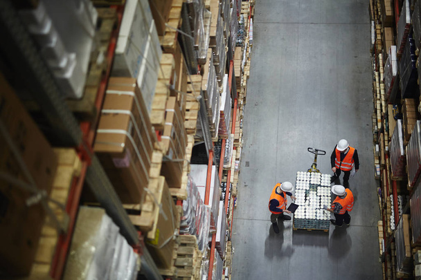 Vista superior de las personas que trabajan en grandes almacenes, contando mercancías en carro móvil entre estantes con cajas embaladas
 - Foto, Imagen