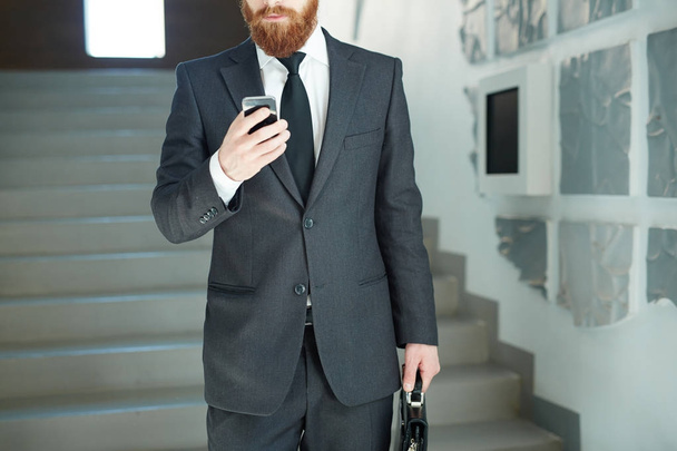 エレガントなスーツや移動中にスマート フォンでネクタイ テキスト メッセージのビジネスマン - 写真・画像