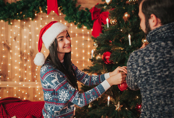 Merry Christmas and Happy New Year . Young couple celebrating holiday at home. Young woman and woman decorate the New Year tree - Fotografie, Obrázek