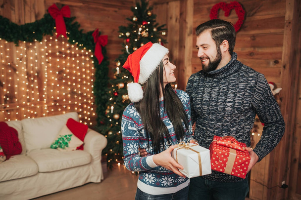 Merry Christmas and Happy New Year . Young couple celebrating holiday at home. Young woman and woman holding gifts in hands - Фото, изображение