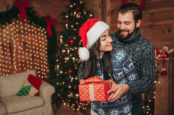 Merry Christmas and Happy New Year . Young couple celebrating holiday at home. Happy young man and woman hug and give each other gifts - Foto, imagen