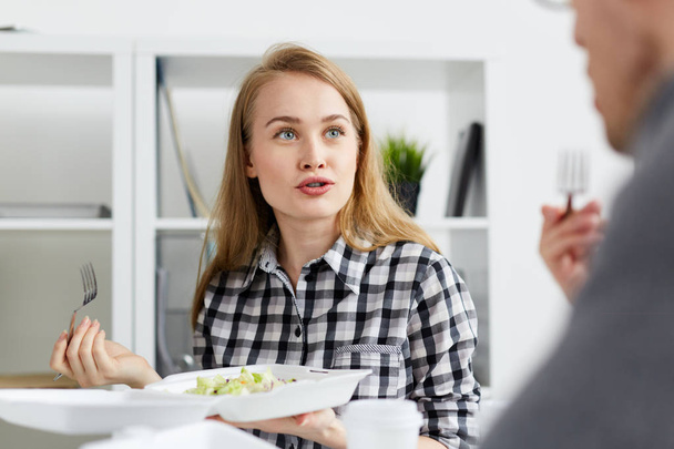 Jeune femme mangeant le repas du récipient et parlant à un collègue au déjeuner
 - Photo, image