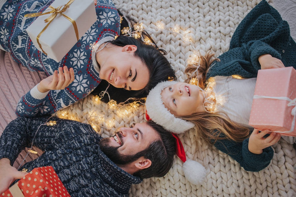 Merry Christmas and Happy Holidays Cheerful Mother, father and her cute daughter girl exchanging gifts. Parent and little child having fun near Christmas tree indoors. Morning Xmas. Portrait family - Foto, Imagen