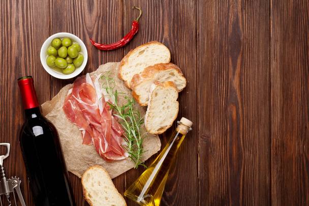 Прошутто, вино, оливки, пармезан и оливковое масло на деревянном столе. Вид сверху с пространством для копирования
 - Фото, изображение