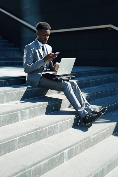 Mobile entrepreneur with laptop and smartphone messaging on stairs - 写真・画像
