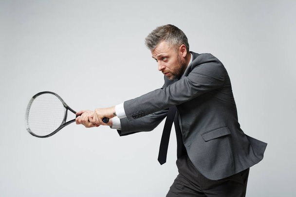 Waist up portrait of confident middle aged businessman countering tennis ball against grey background - Photo, Image