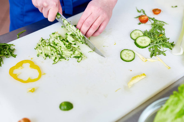 Hands of young trainee with knife cutting fresh cucumbers - Foto, Imagem