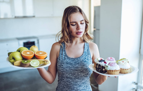 Young woman choosing between fruits and sweets - Foto, Imagen