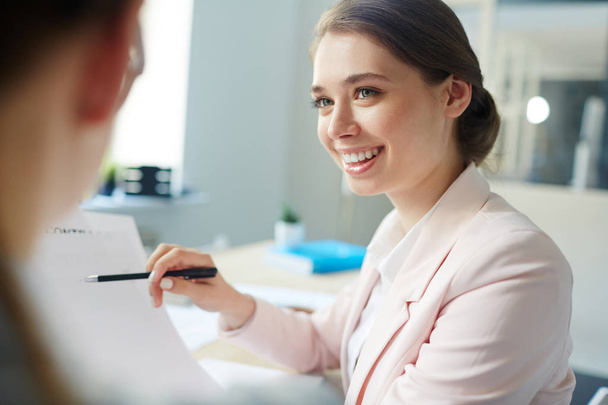 Smiling accountant pointing at financial document in her hand while talking to colleague - Photo, Image