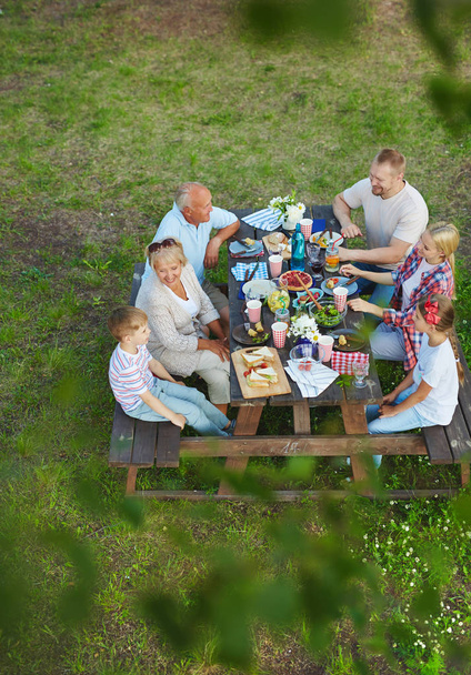 Família feliz sentada à mesa servida no dia de verão
 - Foto, Imagem