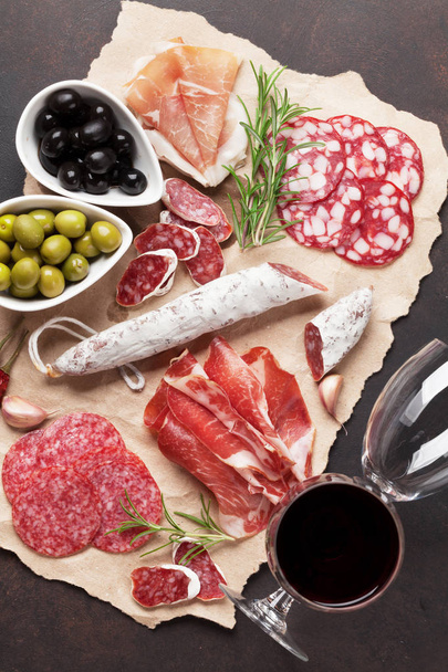 Σαλάμι, κομμένο σε φέτες ζαμπόν, λουκάνικο, προσούτο, μπέικον, ελιές, ψωμί και κόκκινο κρασί γυαλιά. Πιατέλα κρέατος ορεκτικό στο τραπέζι πέτρα. Το Top view - Φωτογραφία, εικόνα