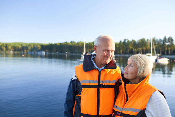 湖で時間を過ごしながら救命胴衣を着て大人のカップル - 写真・画像