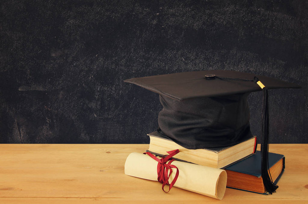 Image of graduation black hat over old books next to graduation on wooden desk. Education and back to school concept - Fotó, kép
