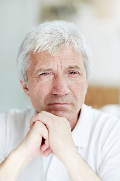 Спокойный мужчина пенсионного возраста пялится в камеру с руками на подбородке
 - Фото, изображение