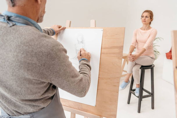 cropped shot of senior man painting on easel and woman posing in art studio - Fotoğraf, Görsel