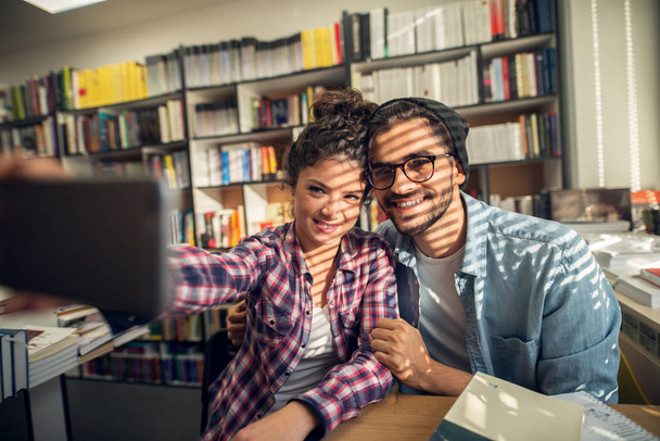 couple of happy young students taking selfie in library - Photo, Image