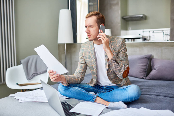 Businessman with paper consulting someone on smartphone during work in home office - Фото, изображение