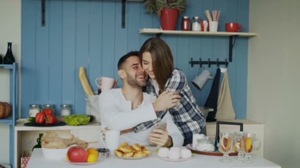 Attractive couple meet in the kitchen at breakfast time and using smartphone for social media surfing at home - Záběry, video