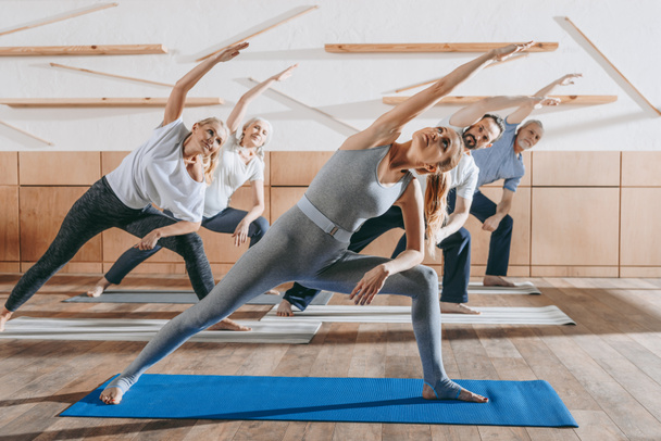 grupo de pessoas idosas praticando ioga e alongamento com instrutor em tapetes em estúdio
 - Foto, Imagem