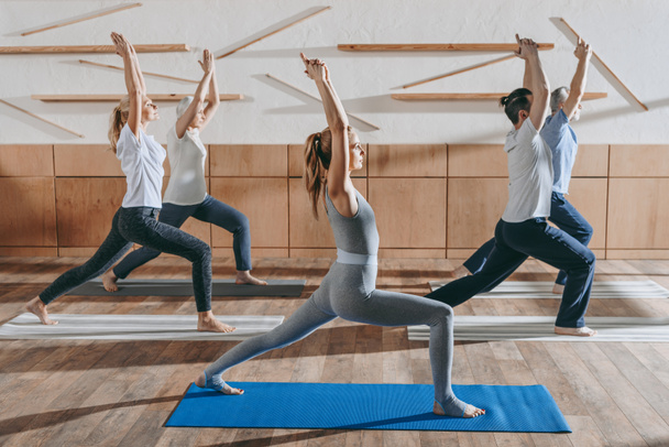 Grup pratik yoga hocası Studio paspaslar üzerinde savaşçı poz ile üst düzey insan - Fotoğraf, Görsel
