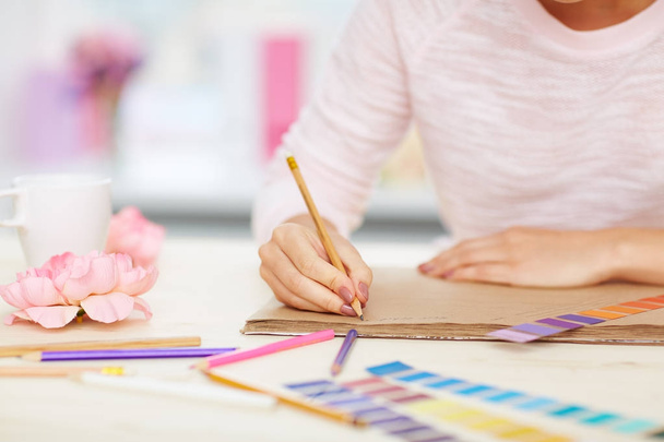 Nahaufnahme weiblicher Hände, die Notizen machen, Farbmuster, Bleistifte und Blumen, die auf weißem Schreibtisch liegen - Foto, Bild