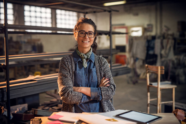 улыбающаяся профессиональная женщина-архитектор позирует с нотами, планшетным ПК и линейками в мастерской
 - Фото, изображение