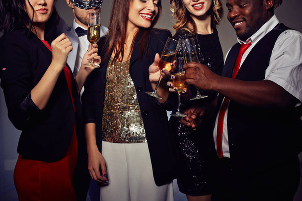 Gros plan de jeunes gens élégants grillant avec des flûtes à champagne tout en se tenant debout sur un fond sombre
 - Photo, image