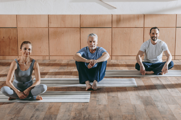 female instructor with mature men sitting on yoga mats and smiling at camera - Foto, Imagem