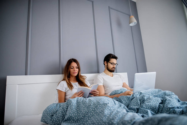atrakcyjne miłości para relaksujący z książki i laptopa przed snem w domu - Zdjęcie, obraz