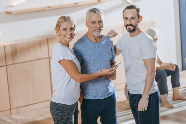 senior people using smartphone and smiling at camera in fitness studio - Fotoğraf, Görsel