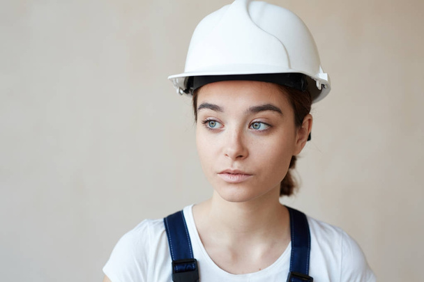 Portrait of female construction worker in hardhat standing against white wall background - Fotografie, Obrázek