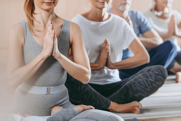tiro recortado de personas mayores con instructor sentado en posición de loto en esteras de yoga
 - Foto, Imagen